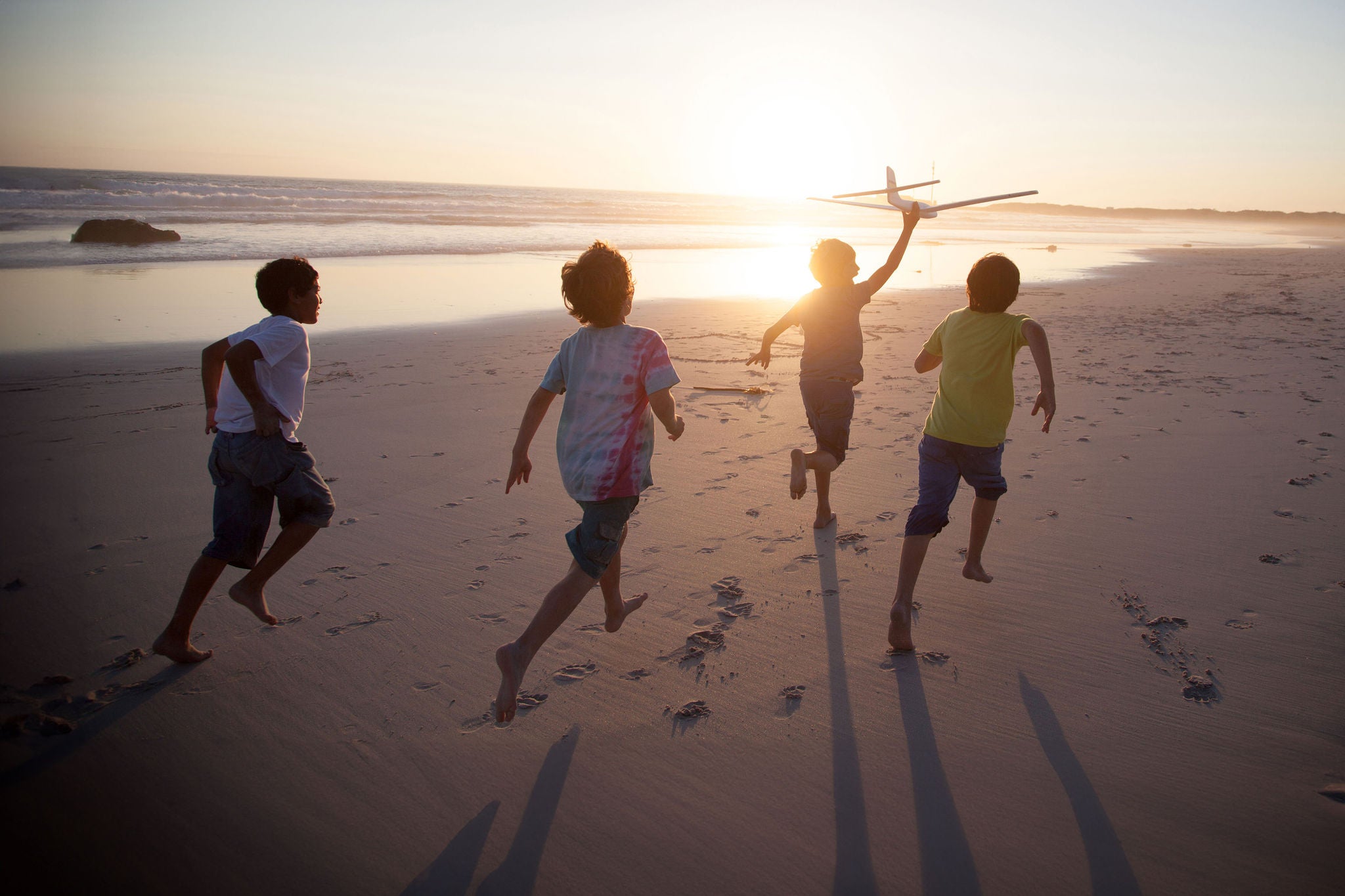 Boys, aged 9-10,  running along a beach at sunset with a toy plane