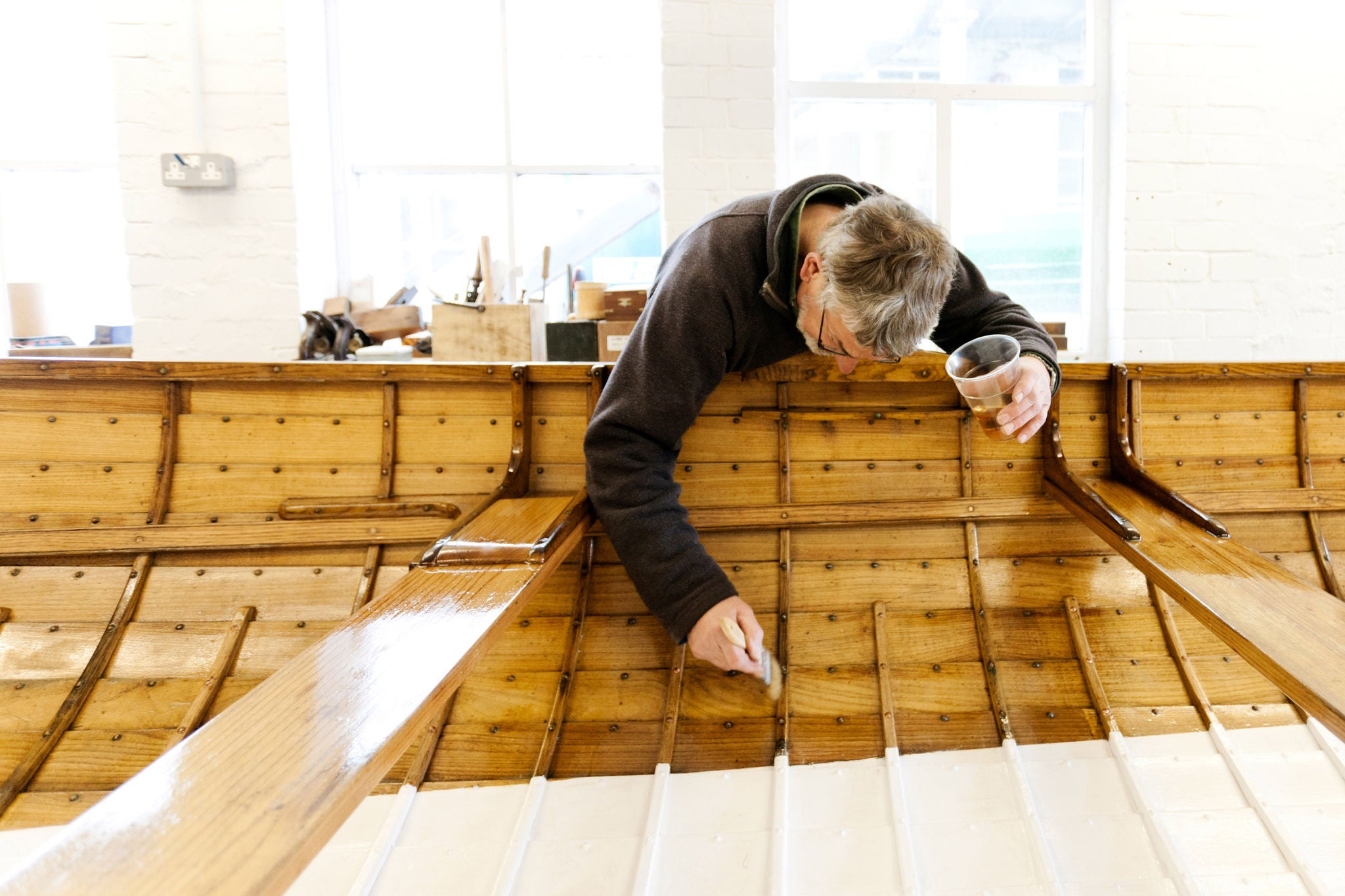 A boat builder paints varnish onto the interior of a traditional, hand built wooden gig boat
