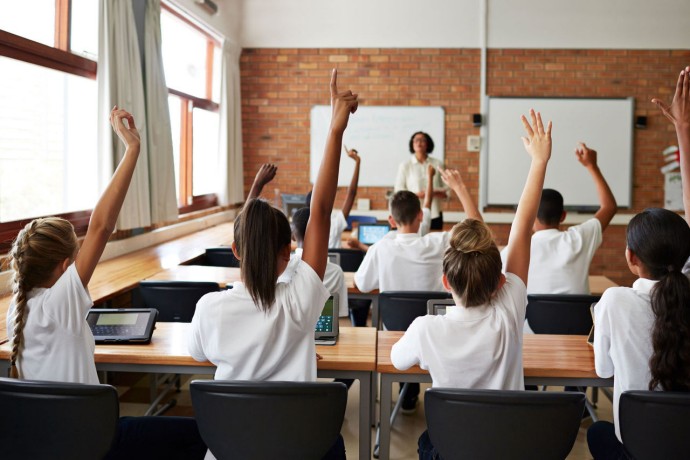 Back view of students in a classroom raising their hands